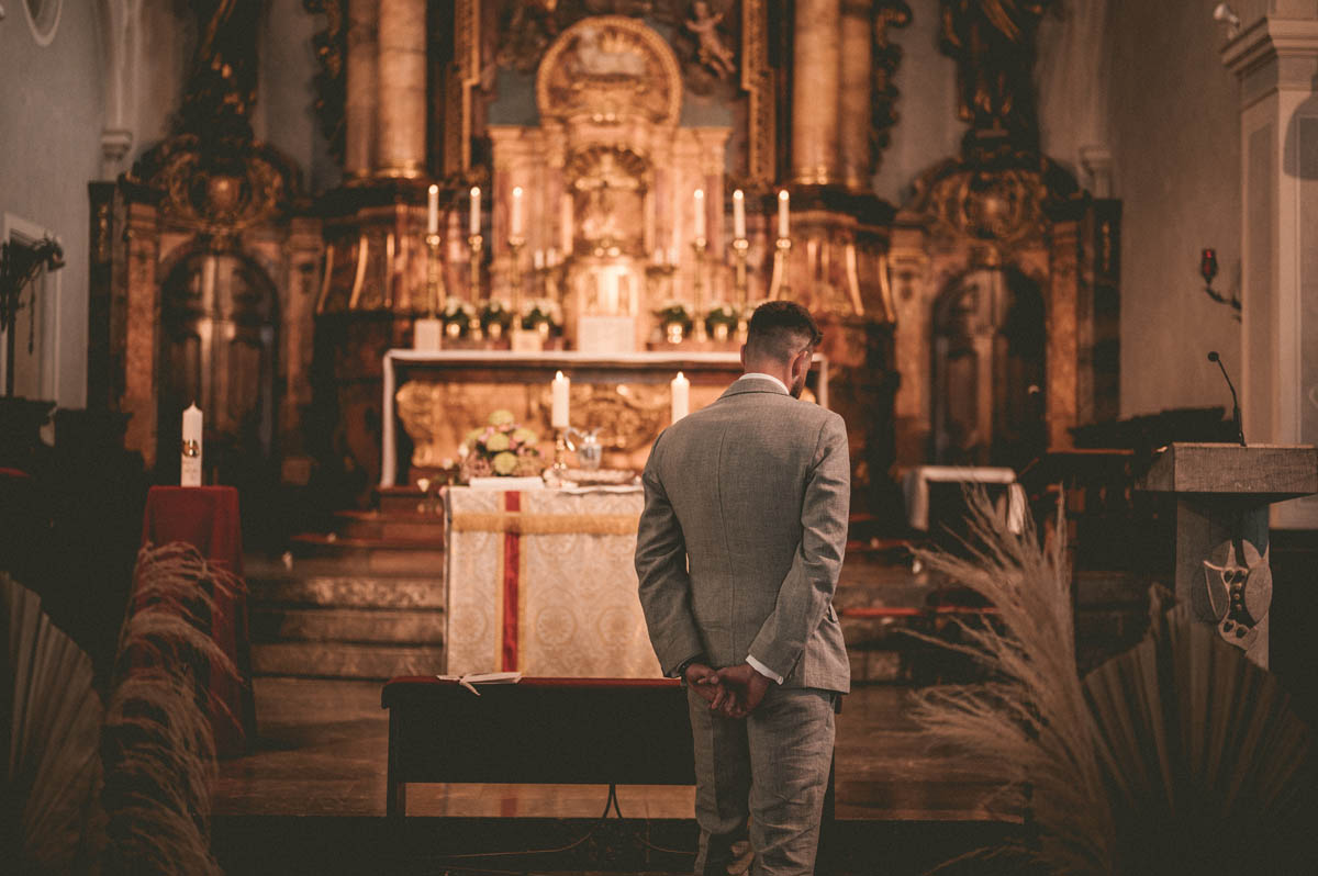 Ein Bräutigam steht mit dem Rücken zum Foto in einer Kirche